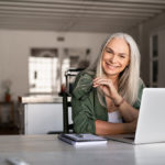 Portrait of happy senior woman holding eyeglasses and looking at camera at home. Successful old lady laughing and working at home. Beautiful stylish elderly woman smiling and relaxing at home.