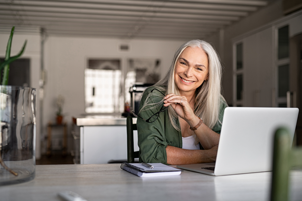 Portrait of happy senior woman holding eyeglasses and looking at camera at home. Successful old lady laughing and working at home. Beautiful stylish elderly woman smiling and relaxing at home.